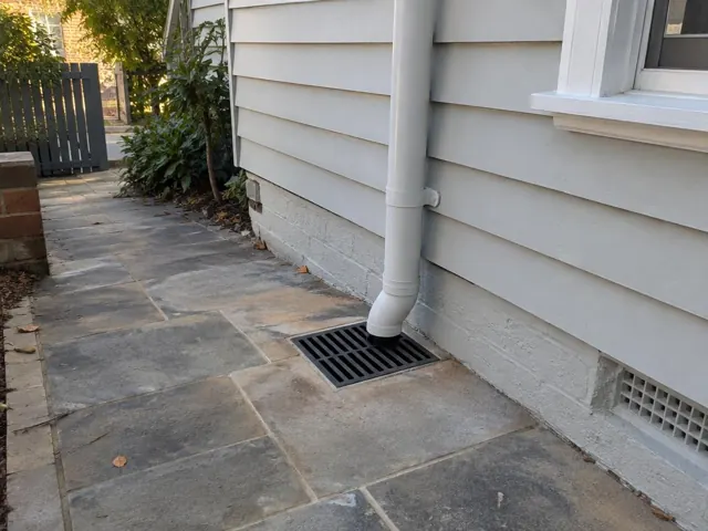 Cleared stormwater grate beside a house wall with dry paved path in Coogee